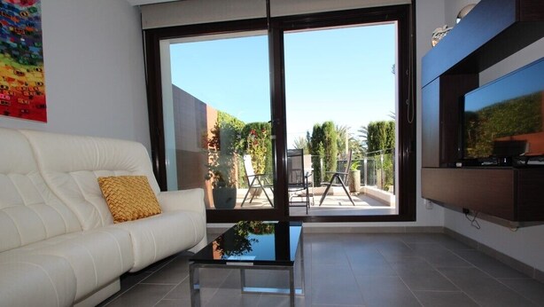 A modern living room with a white sofa, a glass coffee table, and a large sliding glass door leading to an outdoor patio. - Casa D'Alessandro - modern ground floor apartment in quiet neighborhood (Orihuela)