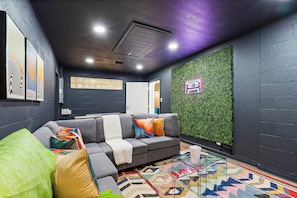 Uma área de estar moderna com um sofá seccional cinza, almofadas coloridas, um tapete estampado e uma parede verde com jardim vertical.