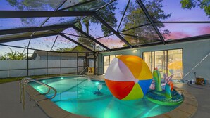 An outdoor swimming pool with a glass enclosure, a colorful beach ball, and a small water fountain. - Clearwater Game House! Heated Pool, Bowling, Golf! (Largo)