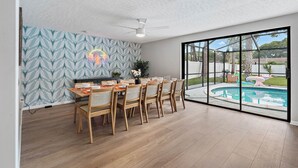 A dining area with a pool view, featuring a modern ceiling fan, patterned wallpaper, and a large glass door leading to an outdoor pool. - Clearwater Game House! Heated Pool, Bowling, Golf! (Largo)