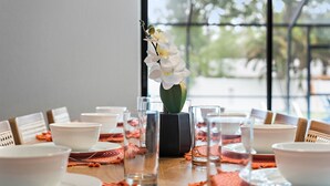 A dining table set with white bowls and glasses, a vase with white flowers, and a view of trees through large windows. - Clearwater Game House! Heated Pool, Bowling, Golf! (Largo)