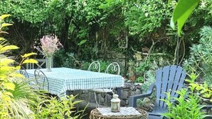 A garden setting with a table and chairs, surrounded by lush greenery and a stone wall. - Apartment in an old mill in a quiet area. Parc des Baronnies. (Aubres)