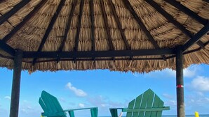 A wooden deck with two green Adirondack chairs facing the ocean under a thatched roof. - Itza Resort (Lighthouse Reef)