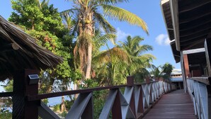 A wooden bridge with a metal railing, leading to a building with a thatched roof. - Itza Resort (Lighthouse Reef)