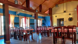 A restaurant with wooden floors, red and white checkered tablecloths, and a brick wall. - Hotel Burans And Restaurant (Chakrata)