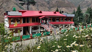 A hotel with a red roof and multiple floors, surrounded by a mountainous landscape. - Hotel Burans And Restaurant (Chakrata)