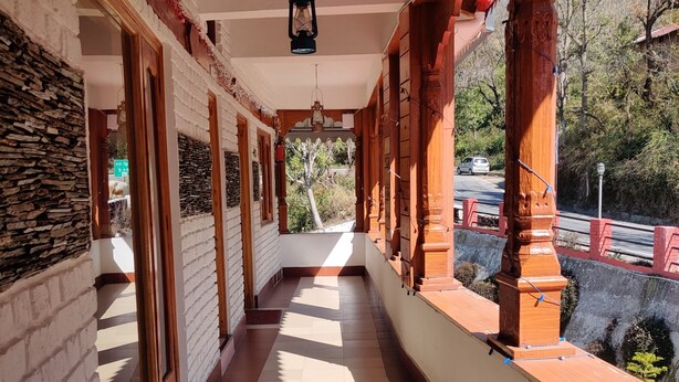 A covered corridor with a tiled floor, wooden columns, and large windows. - Hotel Burans And Restaurant (Chakrata)