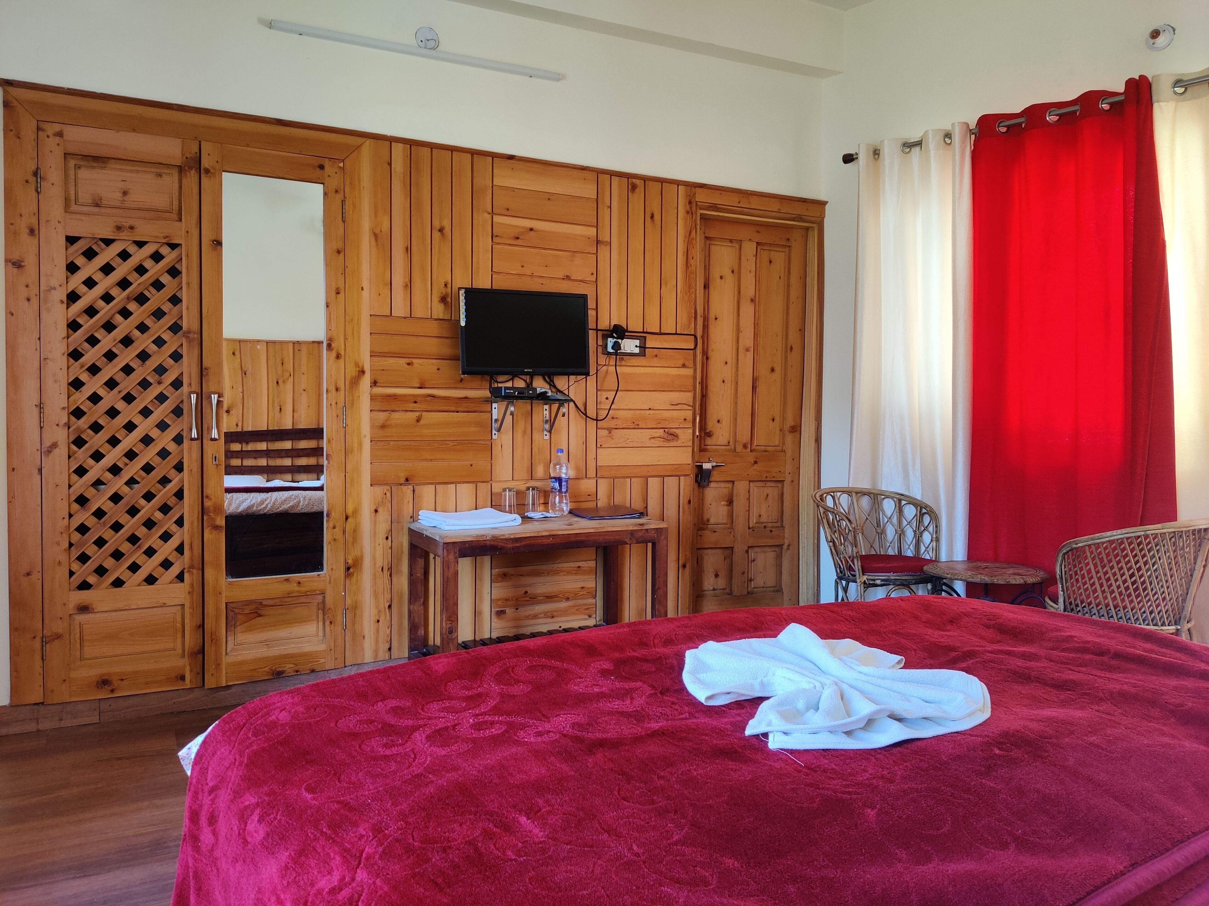 Una habitación con una cama grande, un armario de madera, una mesita con una botella y un televisor montado en la pared.