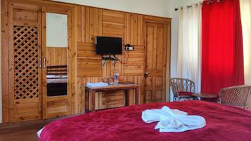 Una habitación con una cama grande, un armario de madera, una mesita con una botella y un televisor montado en la pared.