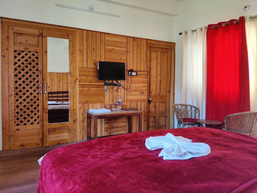 Una habitación con una cama grande, un armario de madera, una mesita con una botella y un televisor montado en la pared.