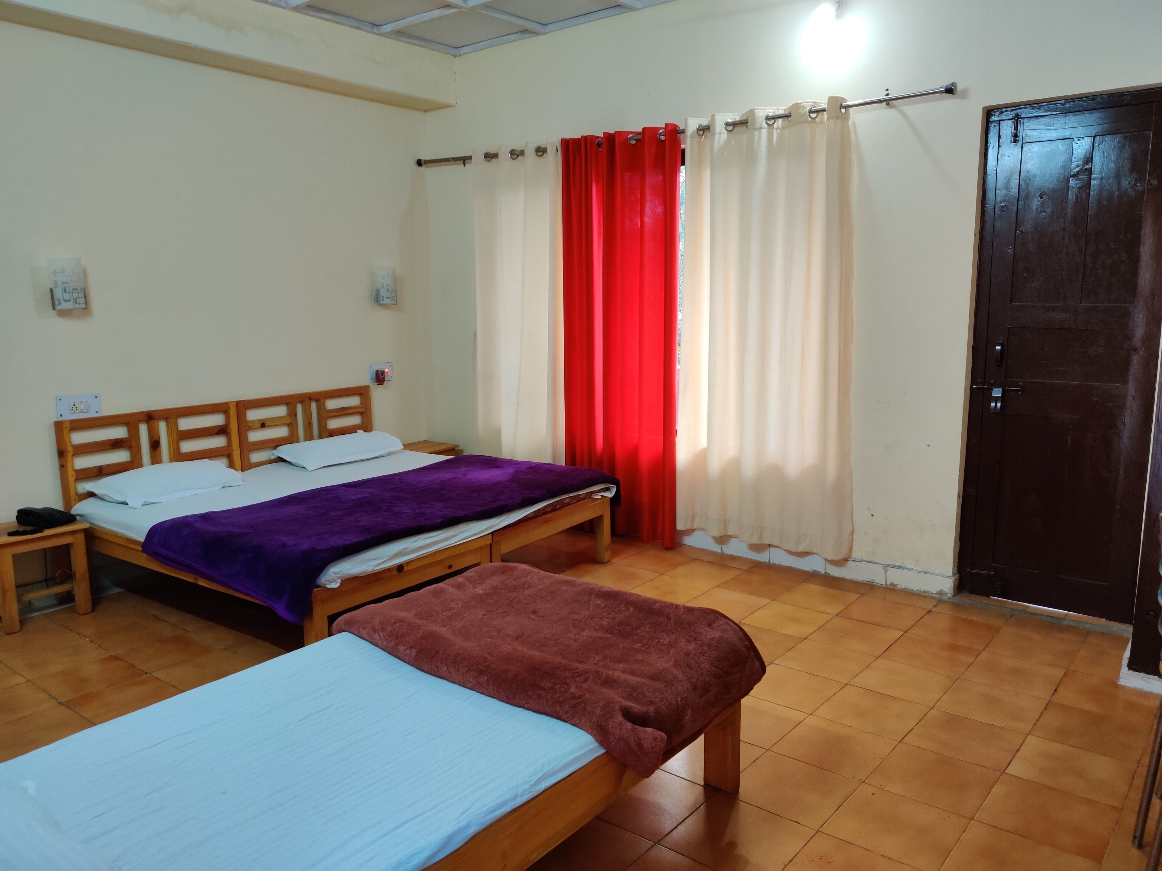 A room with two wooden beds, a red curtain, a white curtain, and a dark wooden door.
