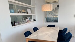Un comedor con una mesa de mármol, sillas tapizadas en azul, un estante de vidrio con adornos y una lámpara colgante moderna.