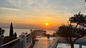 Una terraza en la azotea con vistas a la puesta de sol sobre el mar, una piscina y un árbol en maceta.