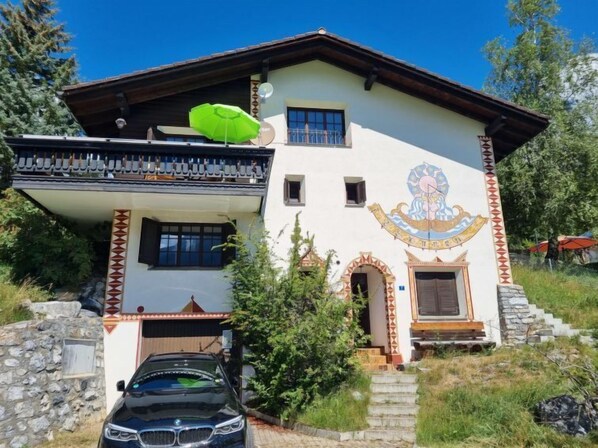 A two-story building with a balcony, a car parked in front, and a mural on the side.