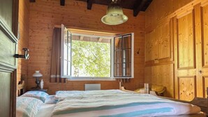 A wooden cabin bedroom with a bed, a nightstand, a lamp, and a large window.