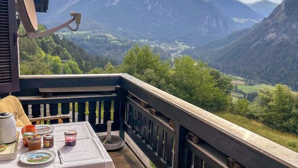 A balcony with a table set for breakfast, overlooking a mountainous landscape.