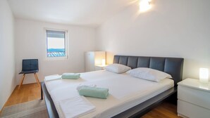 Moderni hotellihuone, jossa on suuri sänky, pieni työpöytä, tuoli, ikkunasta avautuva näkymä ja yöpöytä, jossa on lamppu.