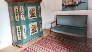 A room with a teal-colored cabinet with floral designs, a bench, and a painting of a coastal scene. - Parkblick by Interhome (Wurzen)