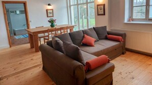 A cozy living room with a brown sofa, a wooden dining table, and a large window. - Parkblick by Interhome (Wurzen)