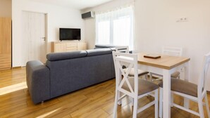 Ein modernes Wohnzimmer mit grauem Sofa, weißen Stühlen, einem Holzesstisch und einem Flachbildfernseher auf einer Holzkommode.