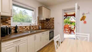 Eine moderne Küche mit weißen Schränken, einem großen Fenster und Blick ins Freie.
