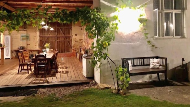 Un espacio de comedor al aire libre rústico con mesas y sillas de madera, un banco y una pérgola cubierta de enredaderas.