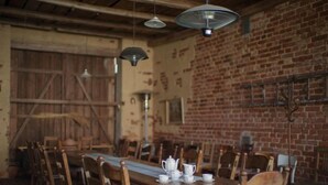Un comedor rústico con mesas y sillas de madera, pared de ladrillo y lámparas colgantes.
