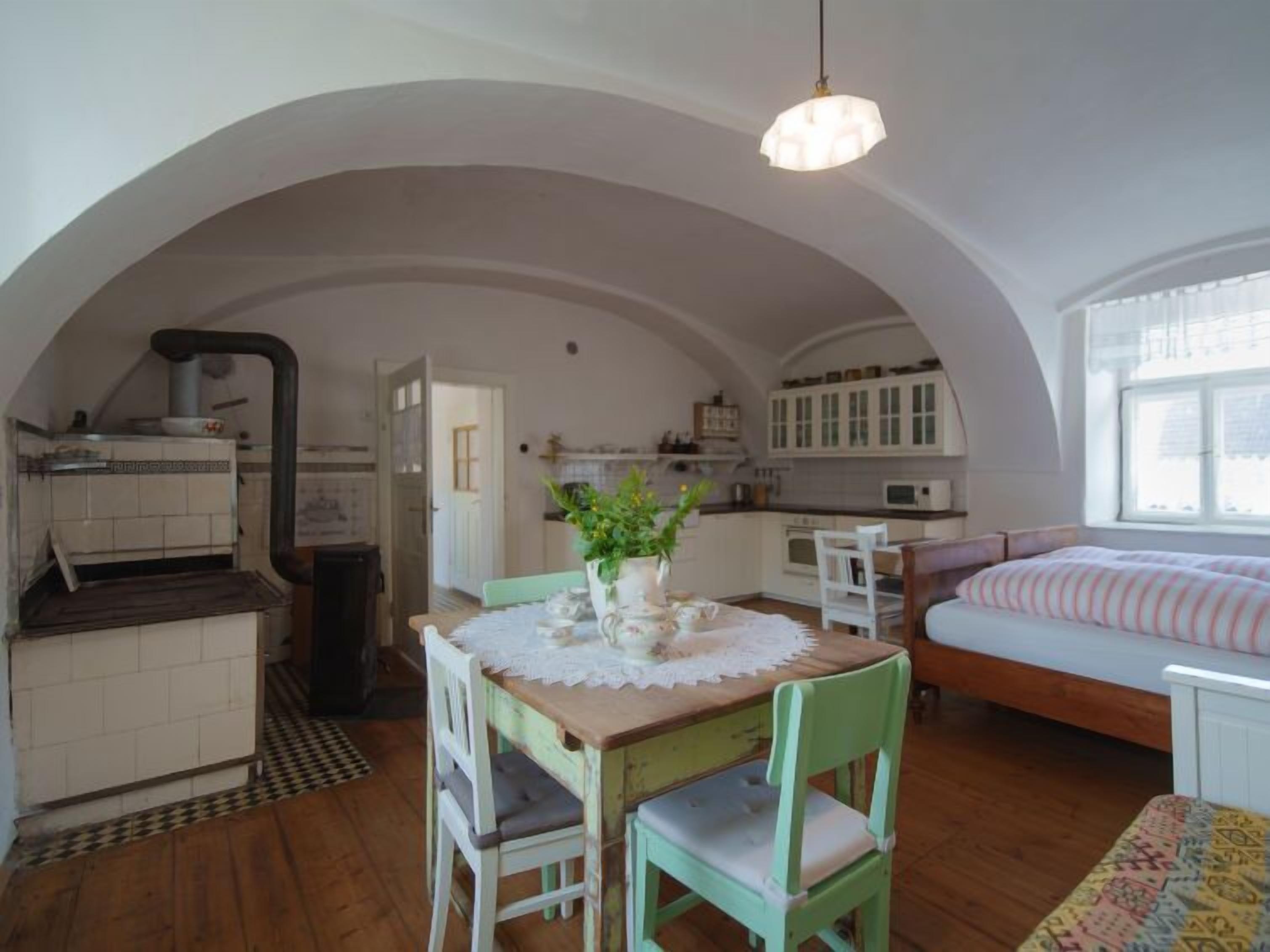 A cozy, compact room with a dining table, chairs, a bed, and a kitchen area.