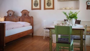 Una habitación acogedora con una cama de madera, una silla verde, una mesa con una planta y dos cuadros en la pared.