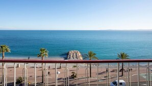 Vista costanera des d'un balcó, amb cel blau, platja i palmeres.
