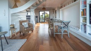 Een ruime woonkamer met een houten trap, een eettafel gedekt voor vier personen en een boekenplank vol boeken.