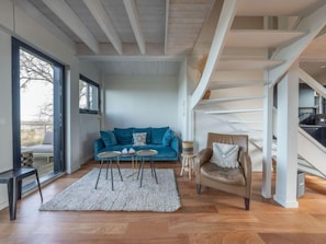 A modern living room with a blue sofa, two small tables, a brown armchair, and a staircase.