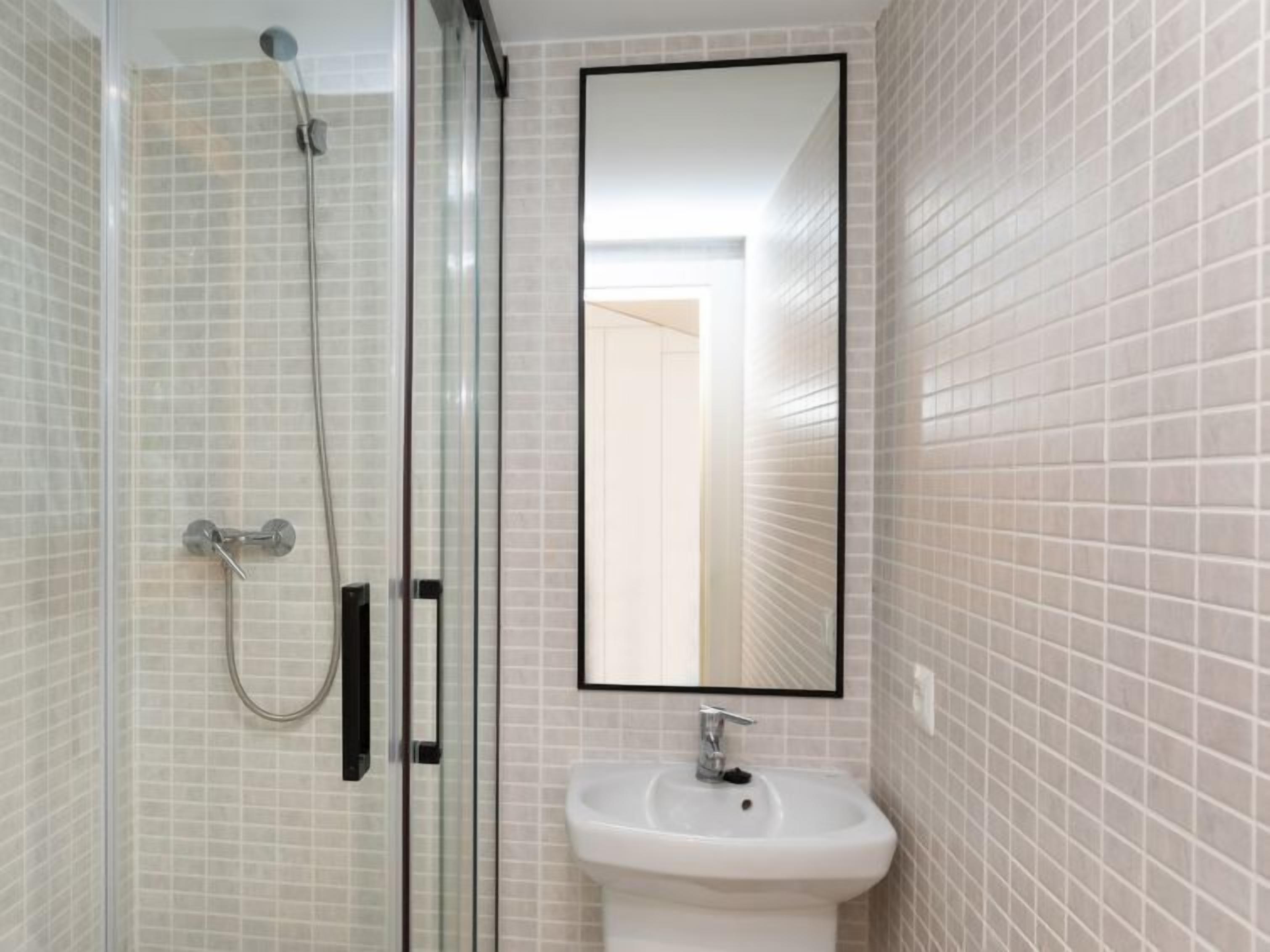 Een badkamer met een douchecabine van glas, een wit wastafeltje en een spiegel.