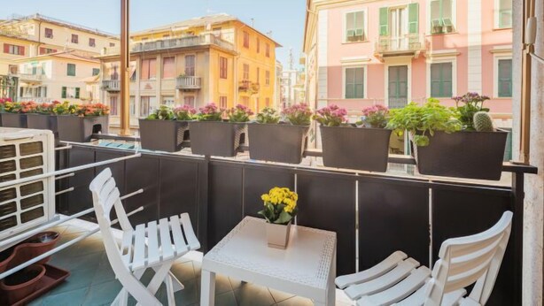 A balcony with white chairs and a table, potted plants, and a view of colorful buildings. - Apartment Blu by Interhome (Rapallo)