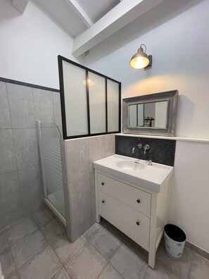 Bathroom features a white vanity with a large mirror, a white sink, and two drawers, along with a black tiled shower area.