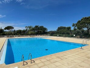 Relax by the serene pool surrounded by lush trees and a clear sky.