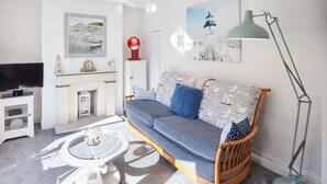 A living room with a sofa, a television, a fireplace, and artwork on the walls. - Host & Stay | Mumbles Cottage (Whitby)