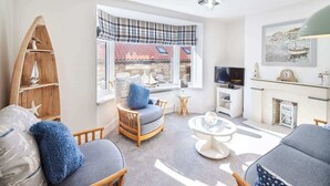A living room with a fireplace, a television, and a window with a view of a building. - Host & Stay | Mumbles Cottage (Whitby)