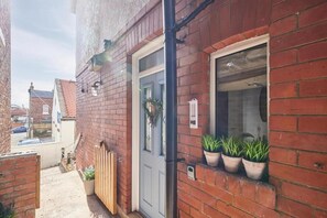 Een smalle steeg met een gebouw van rode baksteen, een houten poort en bloempotten op de vensterbank.
