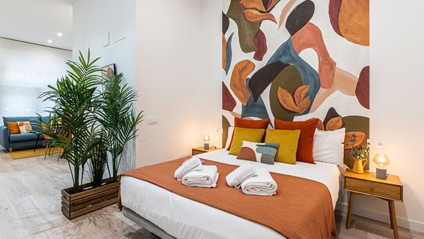 Ett modernt hotellrum med en stor, abstrakt målning på väggen, en säng med ett brunt överkast och en krukväxt.