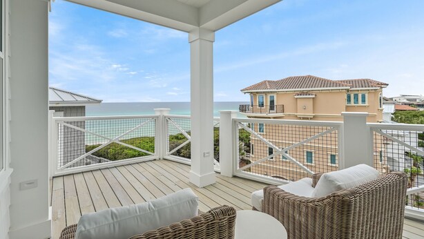 A covered balcony with wicker furniture and a view of the ocean and a house. - Steps From Beach Access + Private Pool- Sunset Lounge by Royal Destinations (Santa Rosa Beach)