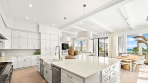 A modern kitchen with white cabinetry, a central island, and a large window offering a view of the outdoors.