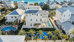 A coastal residential area with multiple white houses, a central swimming pool, and a view of the ocean.