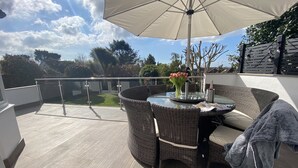 A sunlit outdoor patio with a round table, wicker chairs, and a large umbrella. - Willows Worthing 4 bed With ev Charger & sea Views (Worthing)