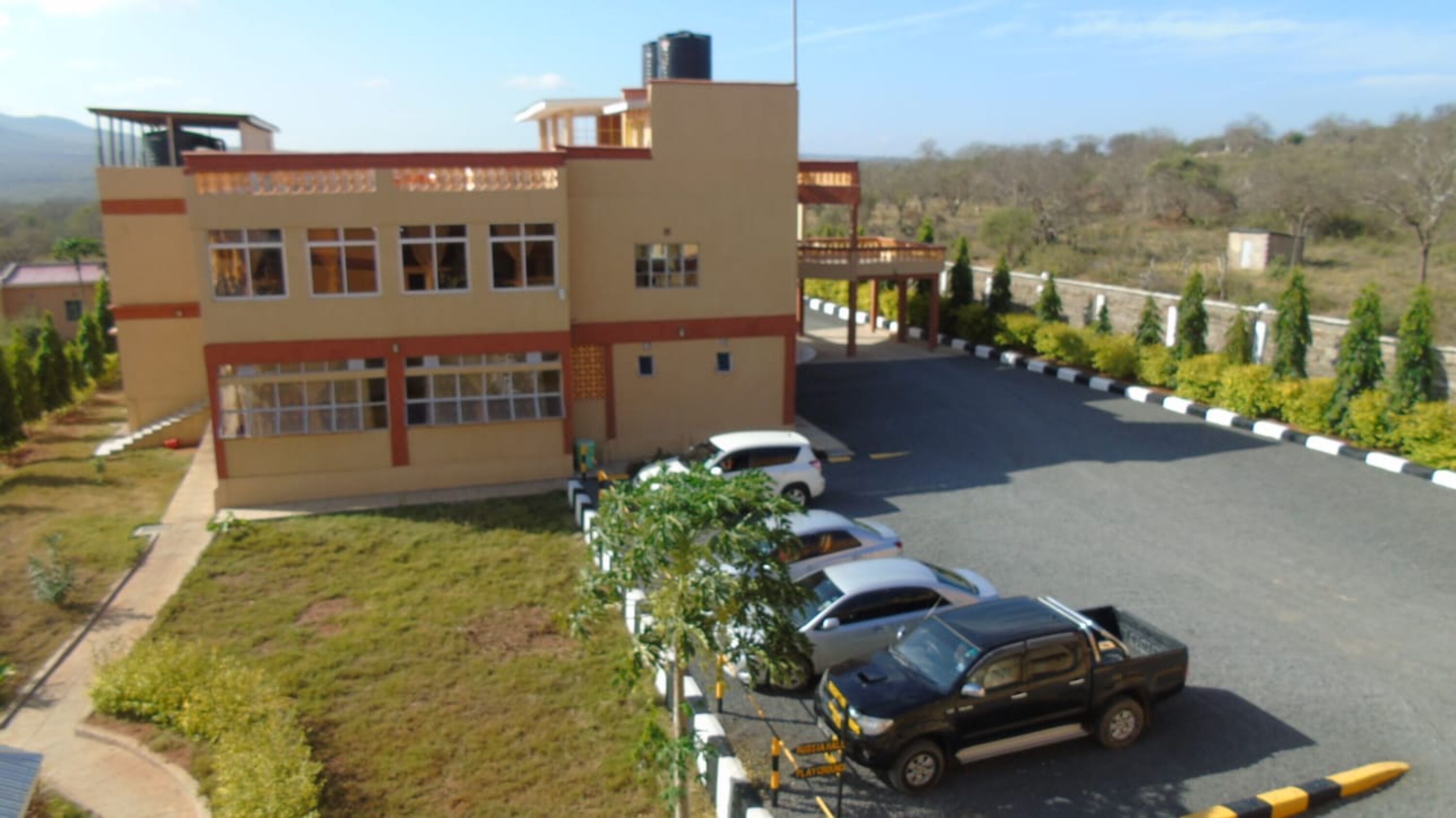 Un edificio de techo plano, con varias ventanas y un estacionamiento con coches.
