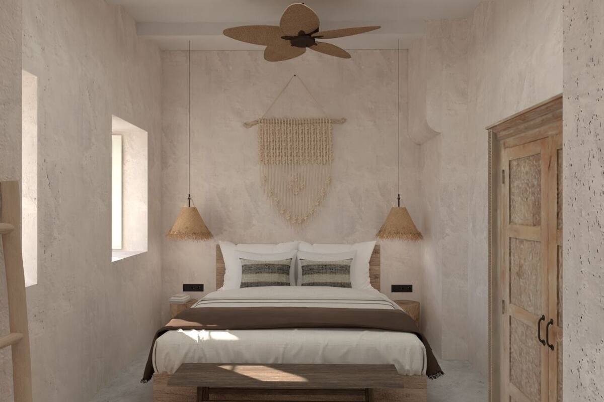 Un dormitorio con una cama, un ventilador de techo, dos lámparas fijadas a la pared, un tapiz tejido y una puerta de madera.