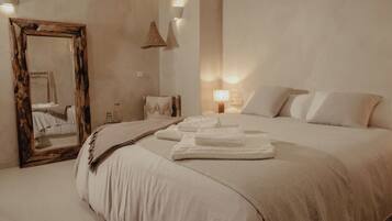 Un dormitorio con una cama grande, un espejo con marco de madera, una mesita de noche con lámpara y un aplique de pared.
