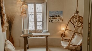 A cozy room with a wooden table, a hanging chair, a window with white shutters, and a wall-mounted lamp. - EntreArcos Casa Eco-Boutique (Vejer de la Frontera)