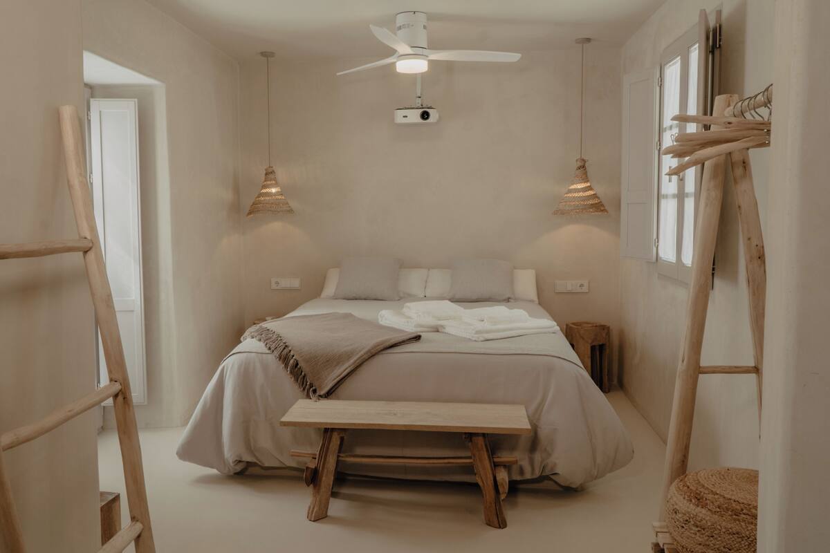 Un dormitorio minimalista con cama, lámparas de noche, ventilador de techo y una escalera de madera.