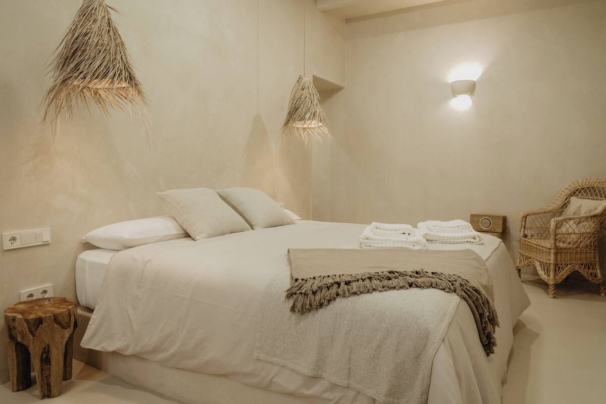 Un dormitorio con cama, mesita de noche y lámpara de mimbre.